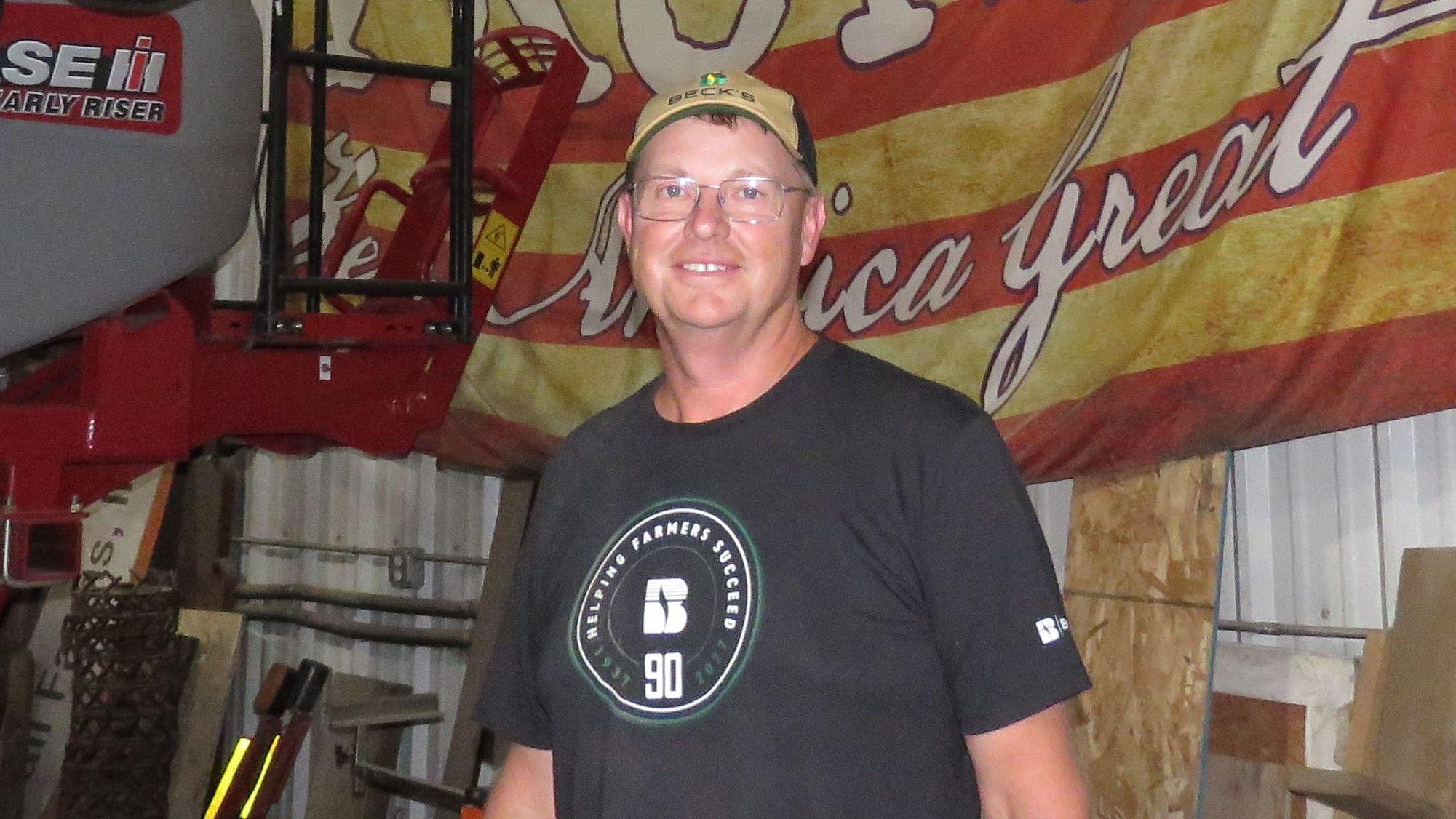 Duane Kimball posa frente a maquinaria agrícola con una gorra y gafas.