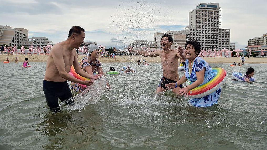 Turistas norcoreanos visitan la playa en la zona turística costera de Wonsan Kalma, en Wonsan, provincia de Kangwon, Corea del Norte, el 2 de julio de 2025. Cuatro personas en traje de baño se salpican agua entre sí.
