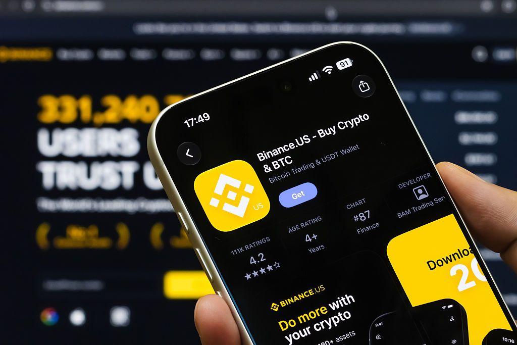 Un teléfono con la aplicación Binance.US junto al logotipo amarillo.