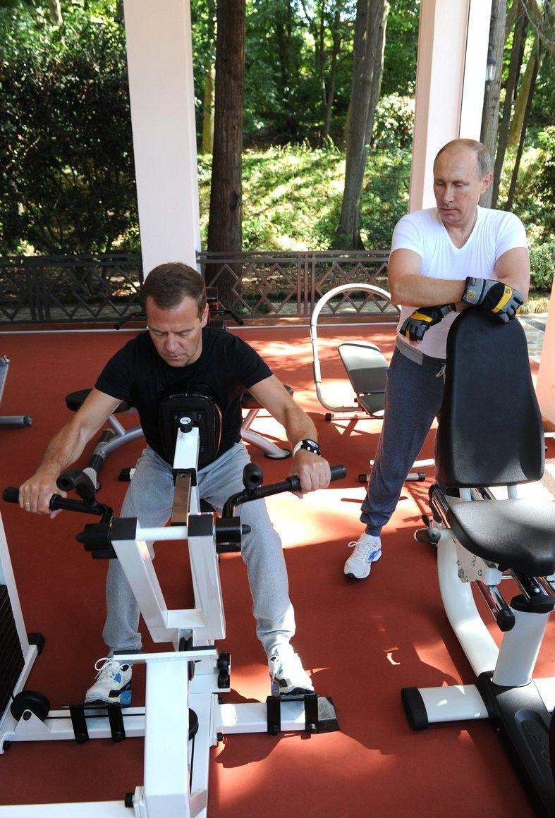 En 2015, el presidente ruso Vladimir Putin aparece apoyado en una máquina de pesas en su gimnasio privado, en su residencia oficial a orillas del mar Negro, en Bocharov Ruchey, Sochi, observando a su entonces primer ministro, Dmitry Medvedev, quien se ejercita sentado en otra máquina. Ambos visten pantalones de chándal grises, zapatillas blancas y camisetas: la de Putin blanca y la de Medvedev negra. Putin lleva guantes de levantamiento de pesas grises, negros y amarillos. Detrás de ellos, una pared de cristal deja ver un claro soleado.