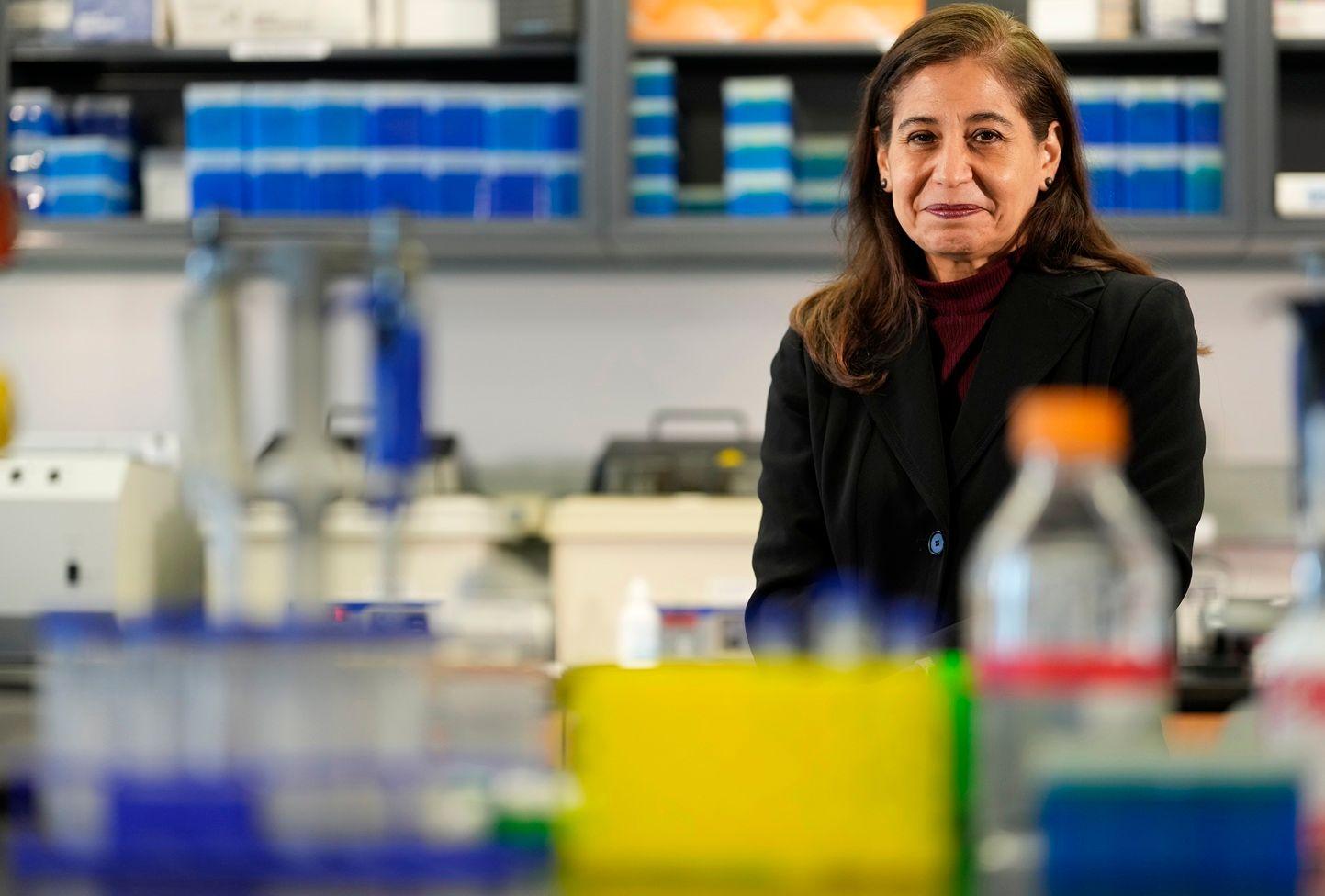 Consuelo Walss-Bass, vestida con un traje negro, está sentada en un laboratorio, rodeada de equipos e intrumentos