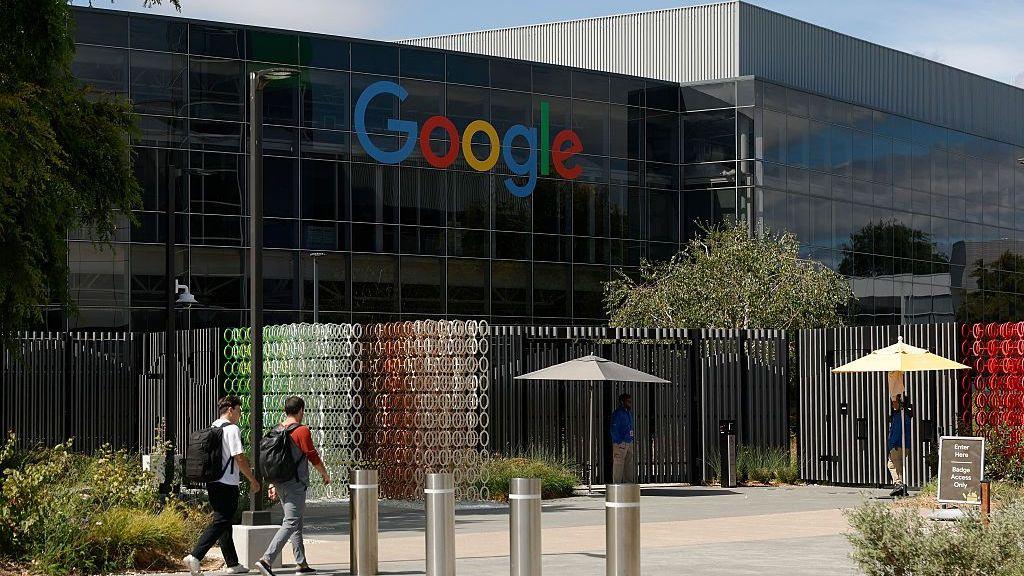 Dos hombres no identificados caminan hacia un enorme edificio con el logotipo de Google en sus ventanas.