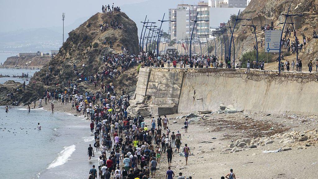 Una fila de decenas de personas, en su mayoría hombres, en la costa de Ceuta. 