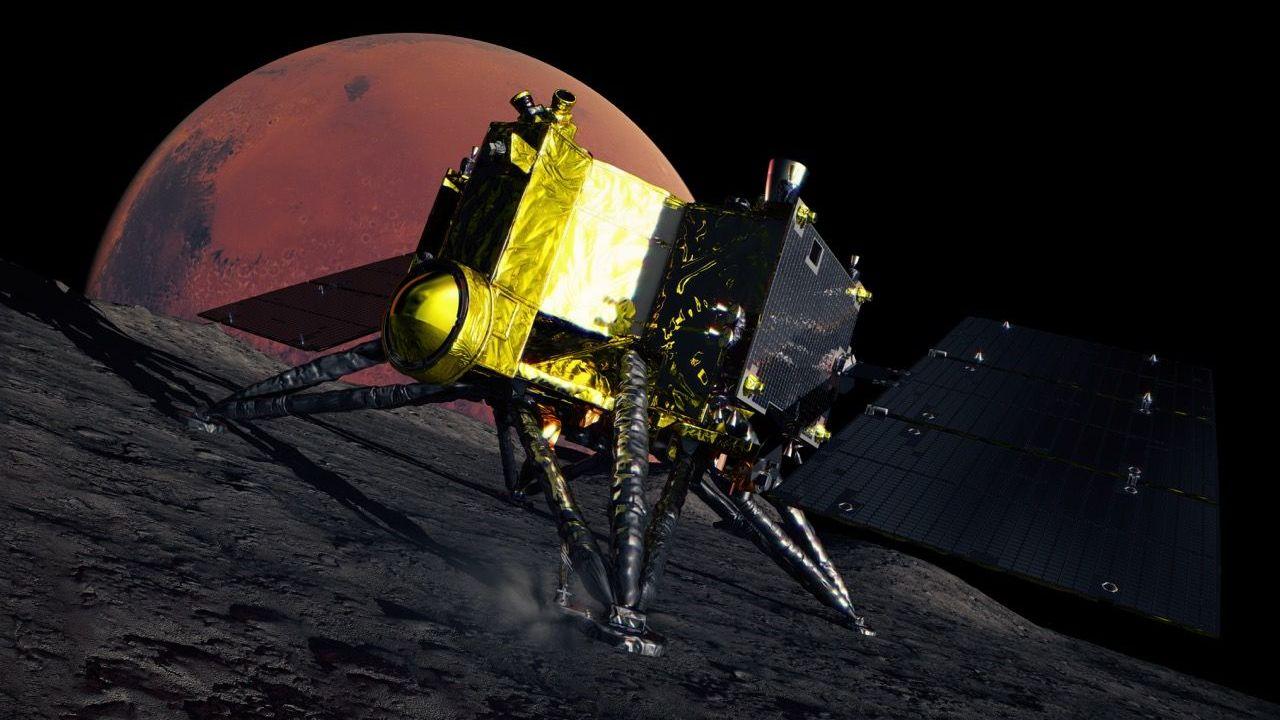 Ilustración artística de la nave espacial MMX sobre la oscura y rocosa superficie de Fobos. La nave es dorada y negra, con cuatro patas triangulares y paneles solares oscuros. Al fondo se aprecia el disco rojo de Marte